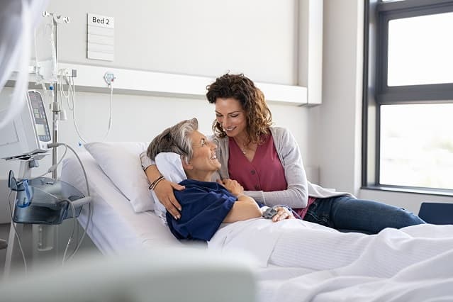 Femme sur un lit d'hôpital avec jeune femme à son chevet