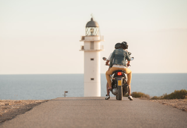 Un homme et une femme sur une moto sur une route qui mène à un phare au bord de la mer