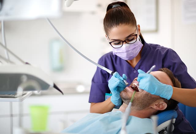Une femme dentiste en train de soigner les dents d'un homme