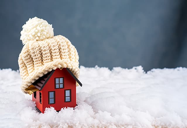Une maison miniature recouverte d'un bonnet en laine, posée sur de la fausse neige