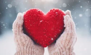 Des mains gantées tenant un coeur rouge en laine avec la neige en arrière-plan