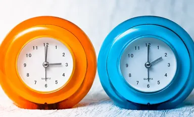 Une horloge orange indiquant 3h, une horloge bleue indiquant 2h pour montrer le passage à l'heure d'hiver