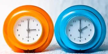 Une horloge orange indiquant 3h, une horloge bleue indiquant 2h pour montrer le passage à l'heure d'hiver