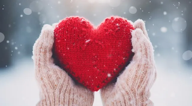 Des mains gantées tenant un coeur rouge en laine avec la neige en arrière-plan