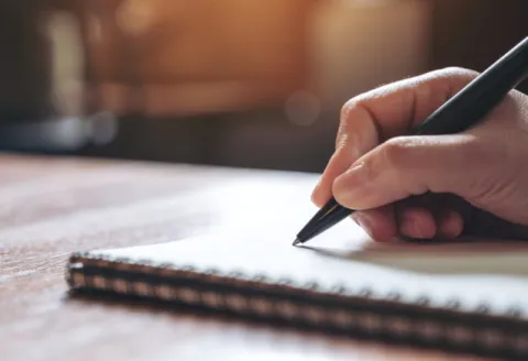Une main tenant un stylo en train d'écrire sur un carnet